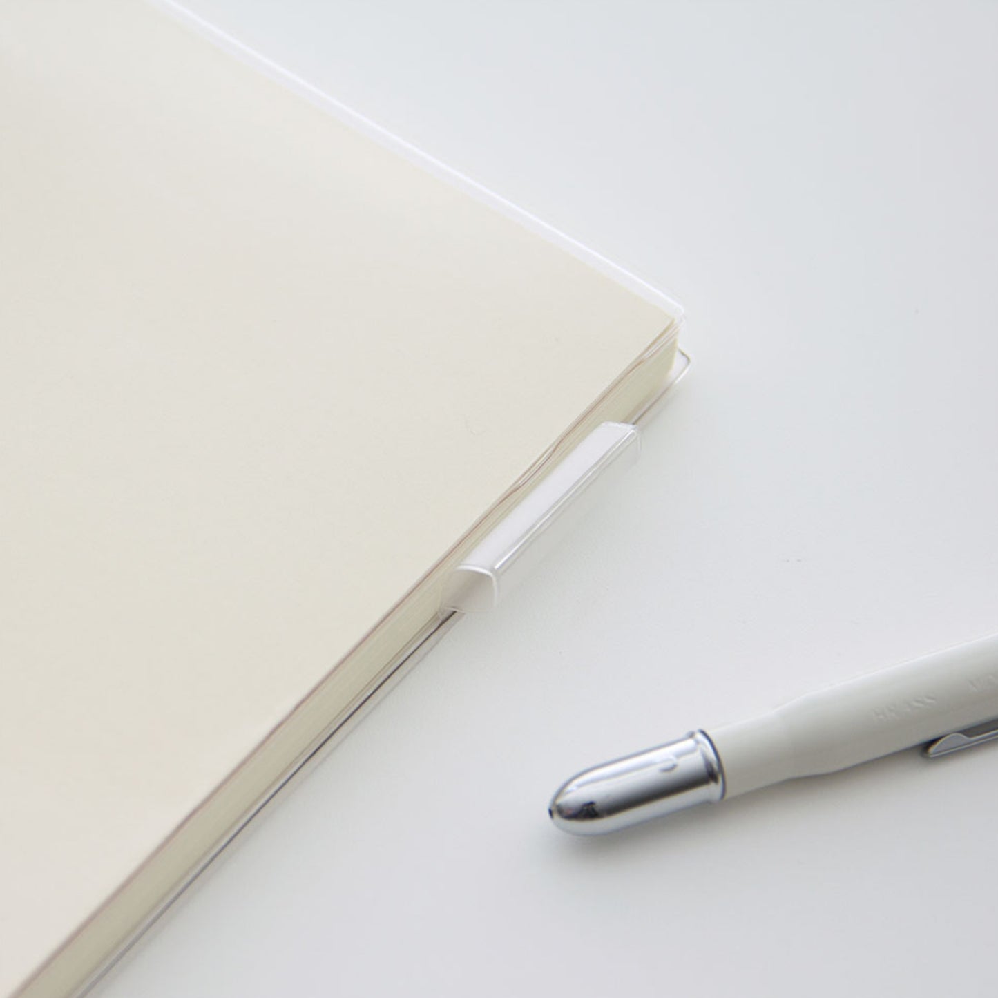 MD A5 notebook with a MD clear PVC protective cover lying on a table showing the clear pen loop on the side.
