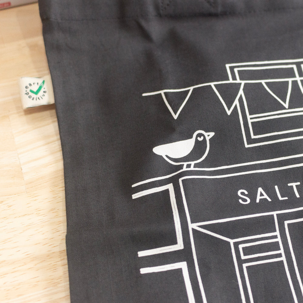 A close up of the design printed onto our Salt Art Supply dark charcoal grey tote bag. The close-up shows the illustration of our shop front and a little seagull sitting on our shop sign.