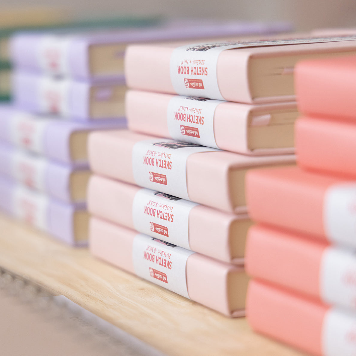 A close up of three stacks of Royal Talens drawing sketchbooks, in colours Pastel Violet, Pastel Pink and Coral Red.
