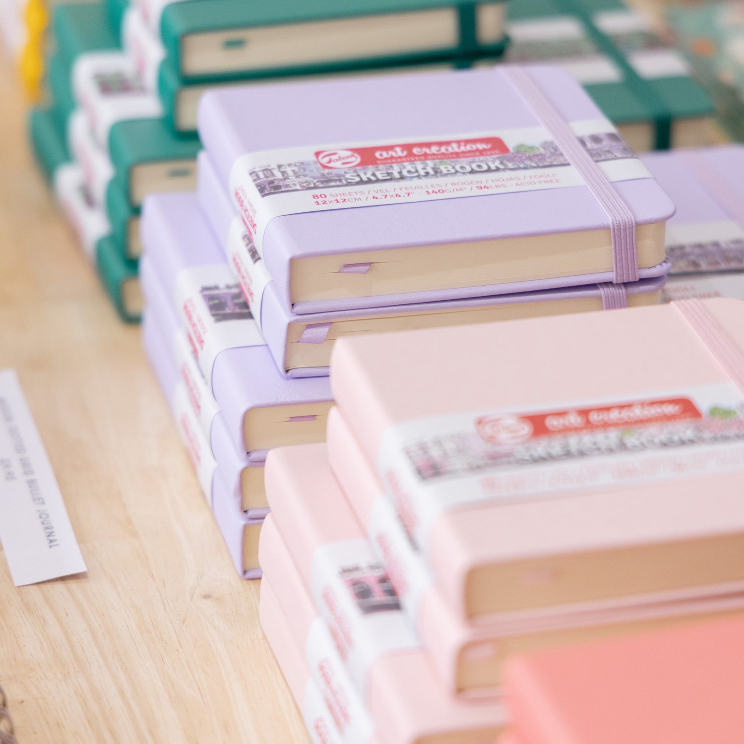 A close up of three stacks of Royal Talens pocket-sized square and landscape sketchbooks. The sketchbook covers are in colours Forest Green, Pastel Violet and Pastel Pink.