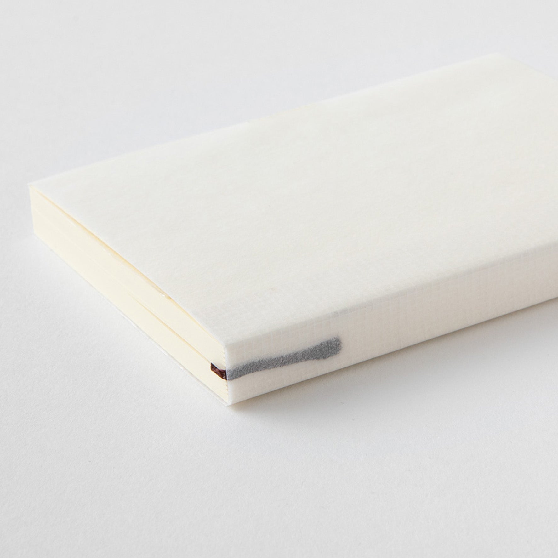 MD paper A7 notebook with minimalist cover an exposed thread spine lying flat on a table. 