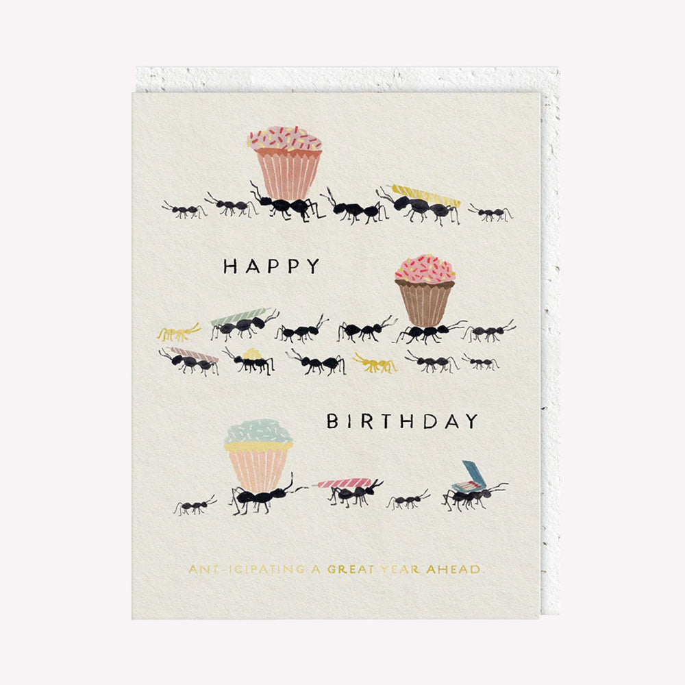 An illustrated greetings card by Seedlings, printed by Ohh Deer. This card features an illustration of ants carrying a birthday cake and candles, with text that reads “Happy Birthday / Ant-ipicating A Great Year Ahead”.