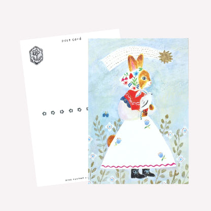 Cozyca Aiko Fukawa postcard design featuring a cat character dressed in a cute outfit holding a bird under a shoorting star on a blue background. The revers features a postcard design with space to write a message. 