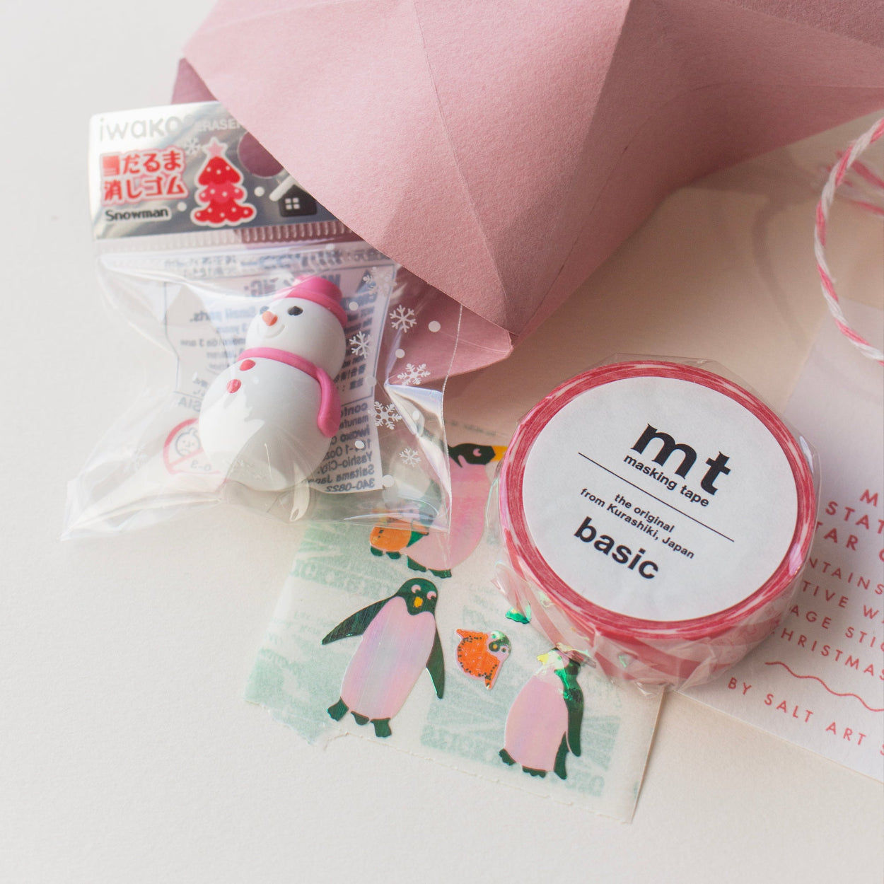 Inside contents of Salt Art Supply's festive stationery star gift box, including a pink snowman shaped eraser, red and white striped washi tape and sheet of vintage penguin stickers.