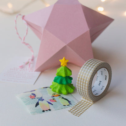 Inside contents of Salt Art Supply's festive stationery star gift box, including a miniature tree shaped eraser, gold gridded washi tape and sheet of vintage penguin stickers. A pink origami star box can be seen in the background.