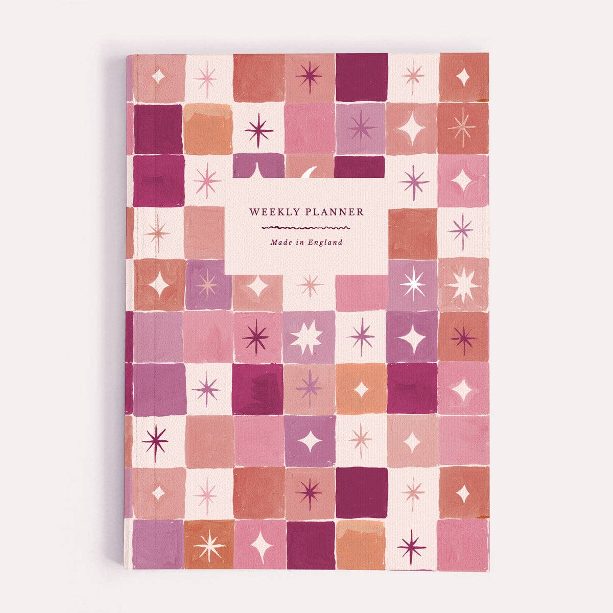 A weekly planner notebook by Sister Paper Co, illustrated with a geometric pink and orange star pattern.