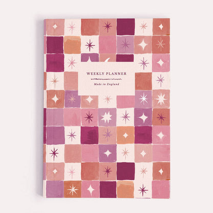 A weekly planner notebook by Sister Paper Co, illustrated with a geometric pink and orange star pattern.