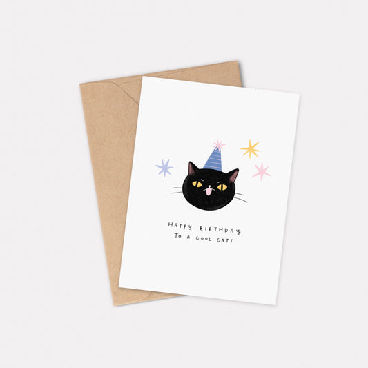 An A6 illustrated card featuring a black cat wearing a blue and pink striped party hat, with the text “Happy Birthday To A Cool Cat” underneath. Stars decorate around the cat face. Behind the card is a kraft brown envelope.