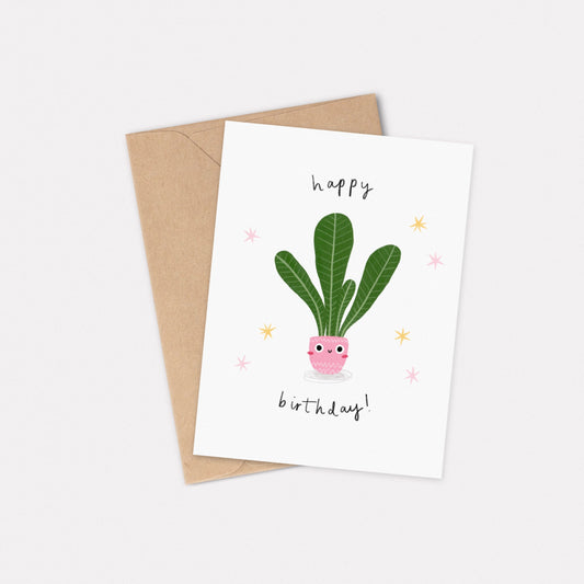 An A6 illustrated card featuring a house plant in a pink pot with a smiley face on. Around the house plant reads “Happy Birthday!”. Behind the card is a kraft brown envelope.