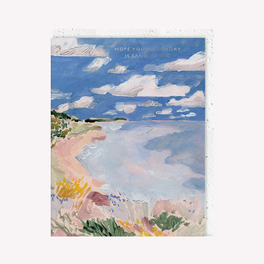 An illustrated greetings card by Seedlings, printed by Ohh Deer. This card features a painted coastal landscape, with text that reads “Hope Your Birthday Is Sand-tastic”.