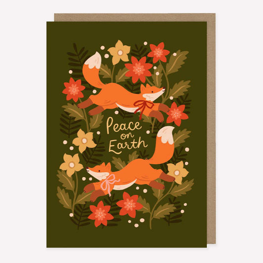 Illustrated Christmas greetings card featuring two foxes and winter foliage on a green background with handwritten text reading "peace on earth". 