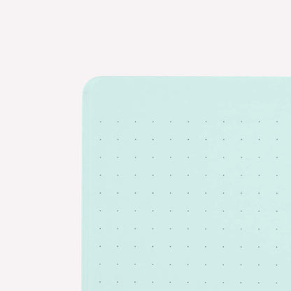Inside corner of a page of the midori soft cover stapled notebook. Pages are pale blue with a subtle dot grid (5mm spacing). 