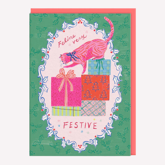 Christmas greetings card featuring an illustrated cat and presents on a green background with a poppy red envelope. Text reads "feline very festive."