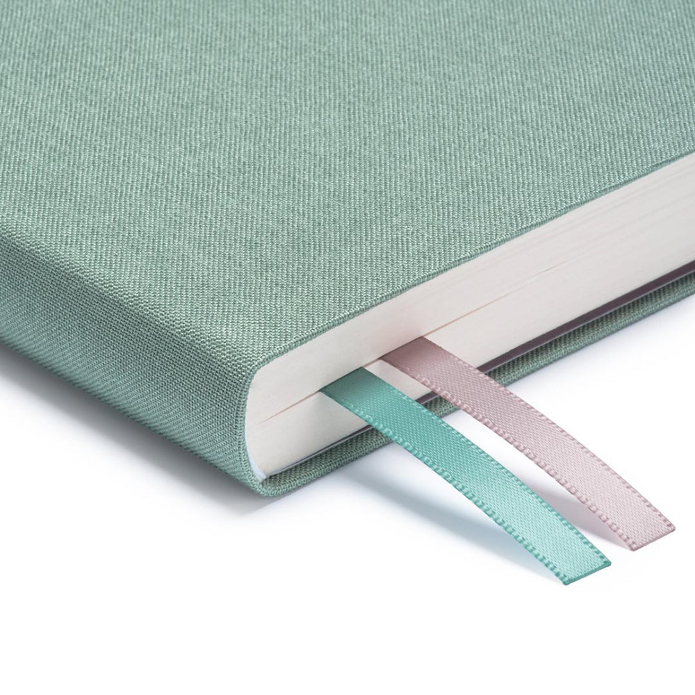 A close up of the corner of Ohh Deer's sage blue daily planner, showing the quality of the linen-style fabric and the two divider ribbons.