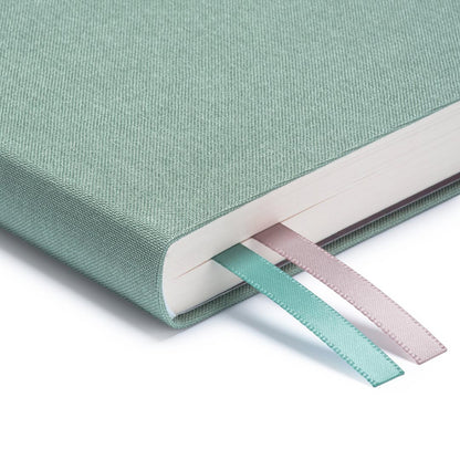 A close up of the corner of Ohh Deer's sage blue daily planner, showing the quality of the linen-style fabric and the two divider ribbons.