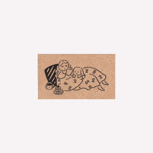 Rubber journalling stam with design of a person and a bunny lying in a blanket with a cup of tea. 