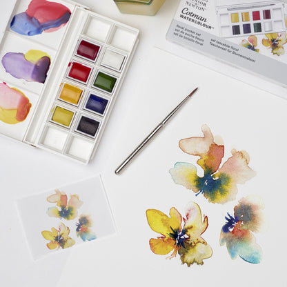A lifestyle photo demonstrating the Cotman Watercolour Floral Picket set in use, with an open palette showing the 8 half pan paints included in this set, alongside a painting of flowers to show the type of work this palette has been curated for. 